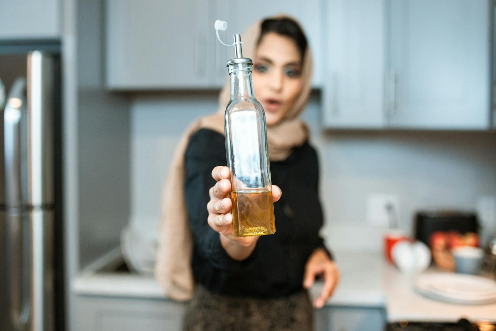 Ethnic woman demonstrating bottle of sunflower oil while cooking